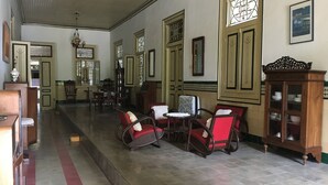 Een ruime hal met rode en bruine stoelen, een houten kast met glazen deuren en een groot raam met ingewikkelde decoraties.