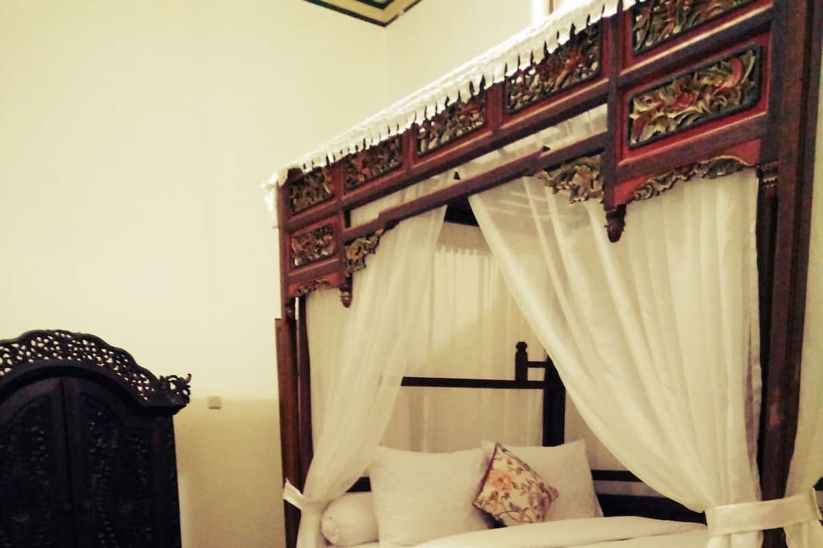 A traditional four-poster bed with a canopy, a wooden chair, and a patterned rug.