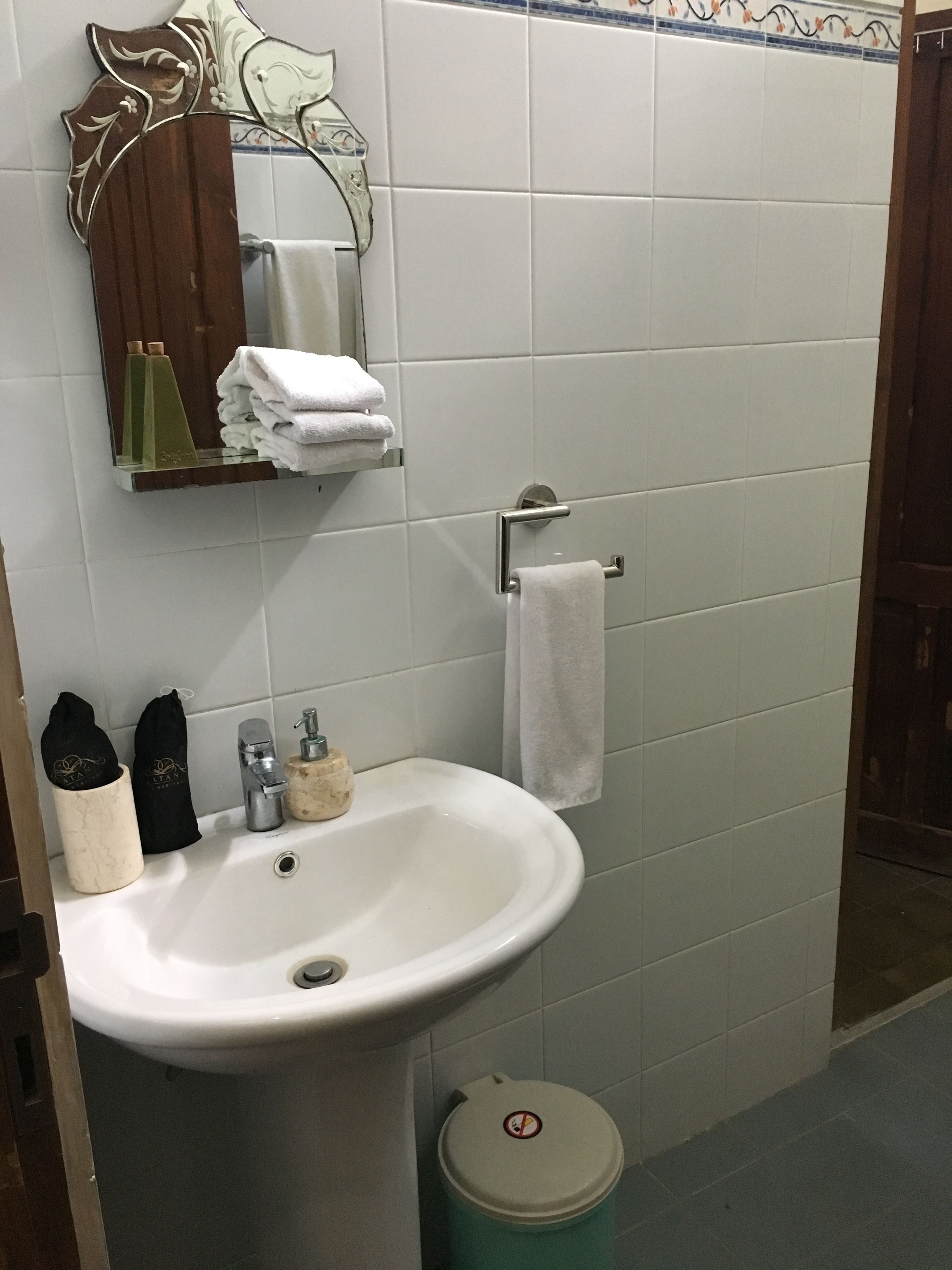 Casa de banho com lavatório branco, espelho, porta-toalhas e um cesto de lixo.