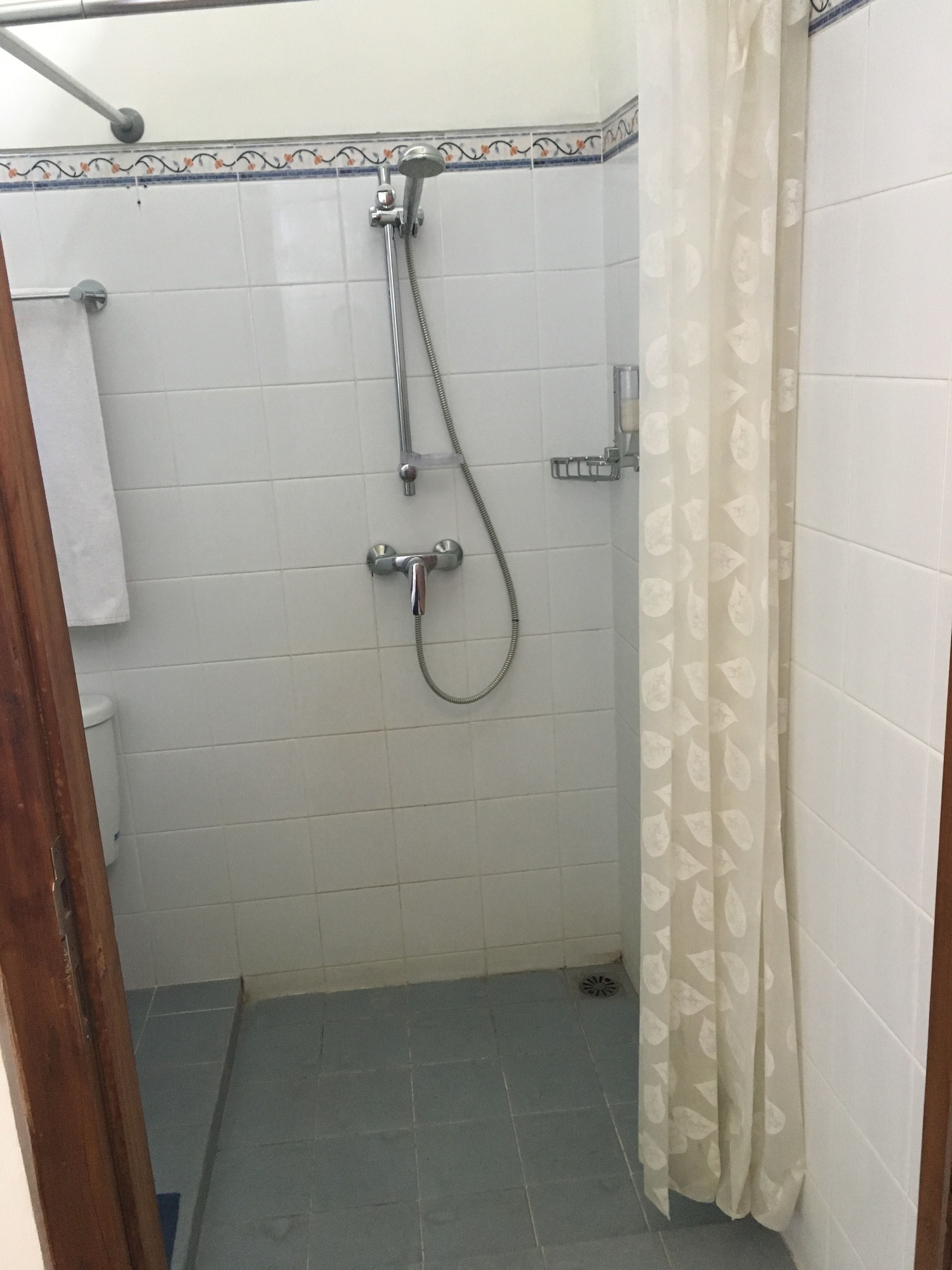 Un espacio de ducha pequeño con azulejos, un cabezal de ducha, un rociador de mano y un inodoro.