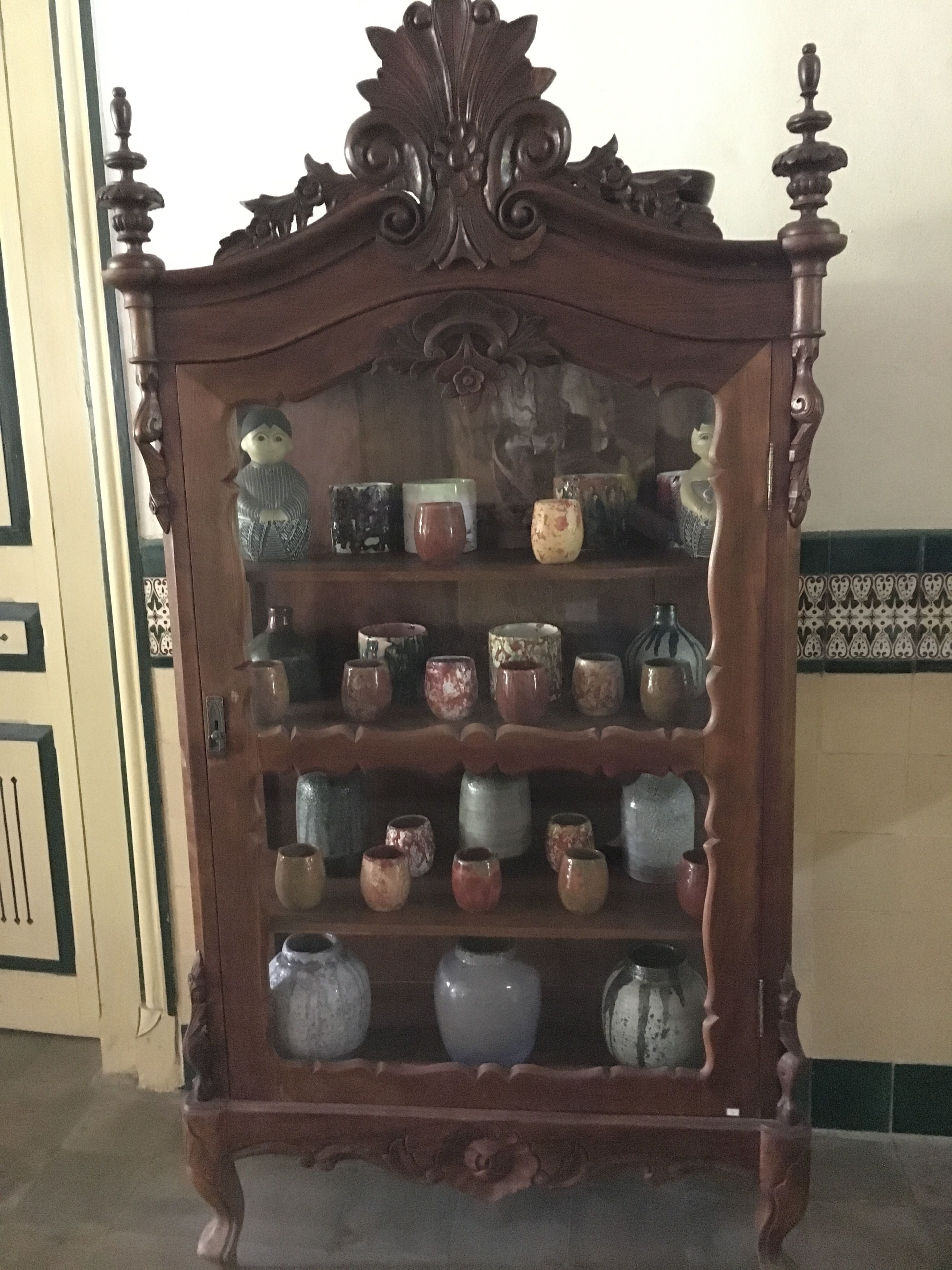 A wooden cabinet with ornate carvings and multiple shelves holding various ceramic items.
