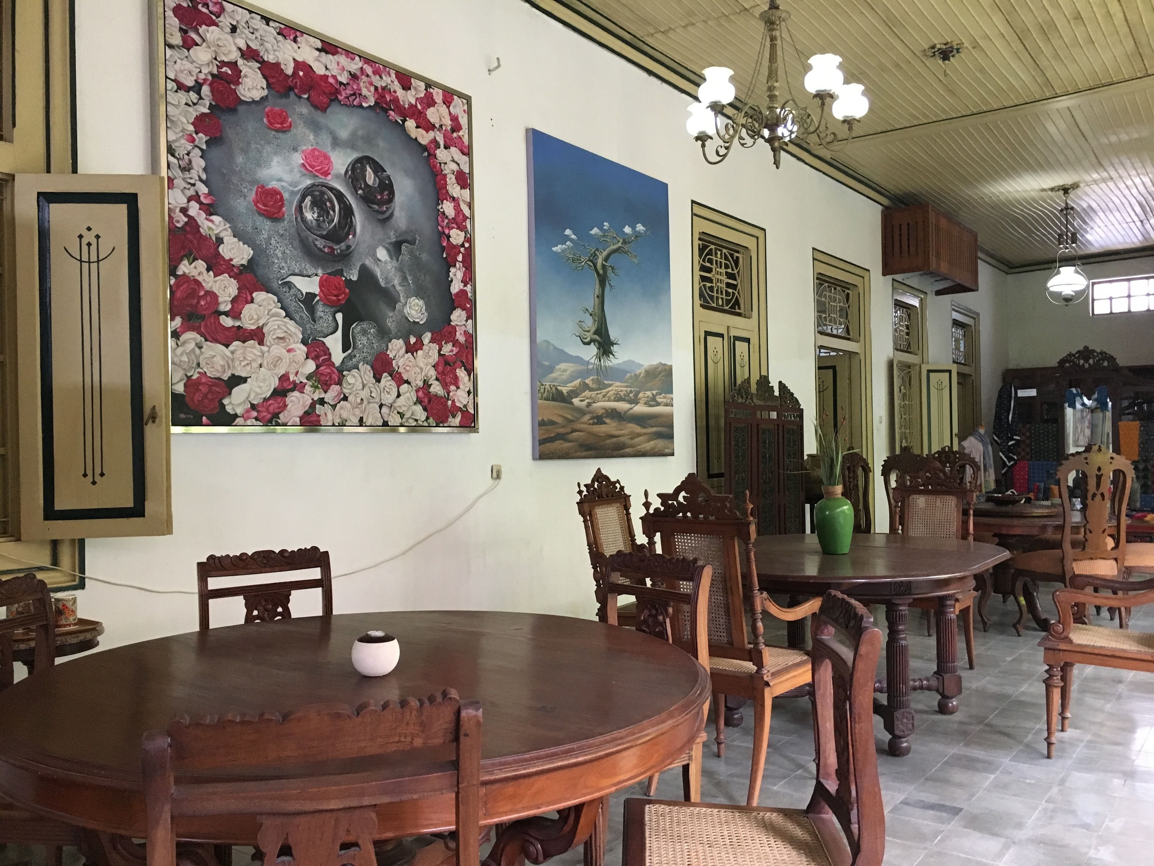 Un comedor con mesas y sillas de madera, una araña y obras de arte en las paredes.