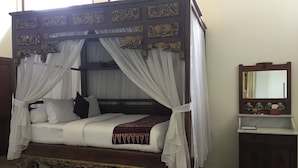 Een hemelbed met een baldakijn, een houten nachtkastje en een spiegel.