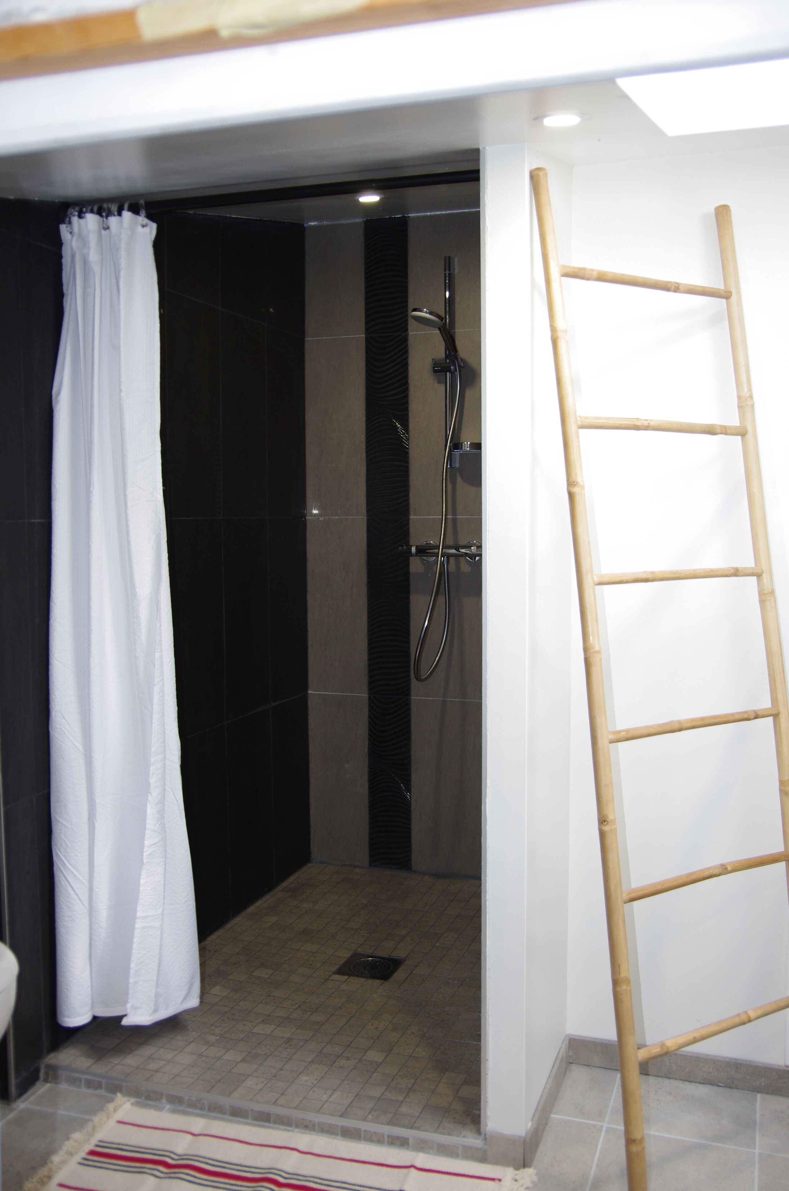 A shower area with a bamboo ladder, a white shower curtain, and a tiled floor.