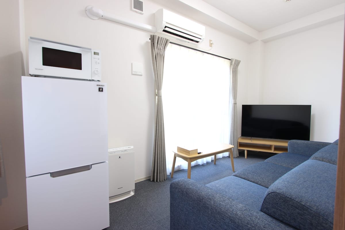 A modern living room with a flat-screen TV, a microwave, a refrigerator, and a sofa.