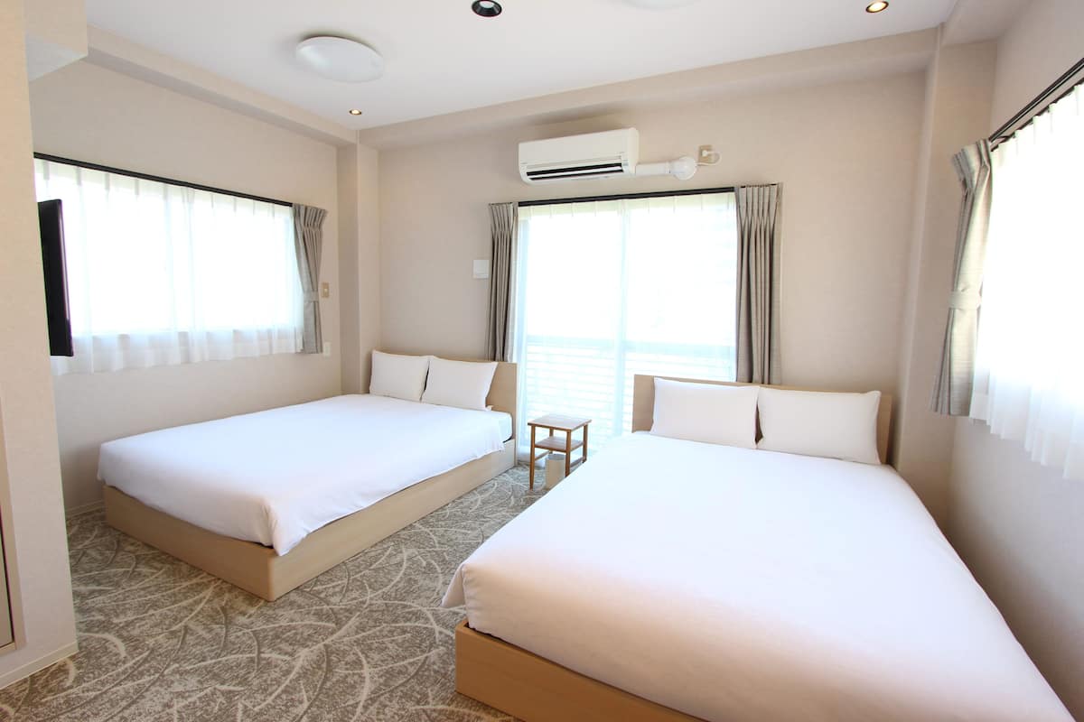 A hotel room with two single beds, a small table, and a large window with curtains.