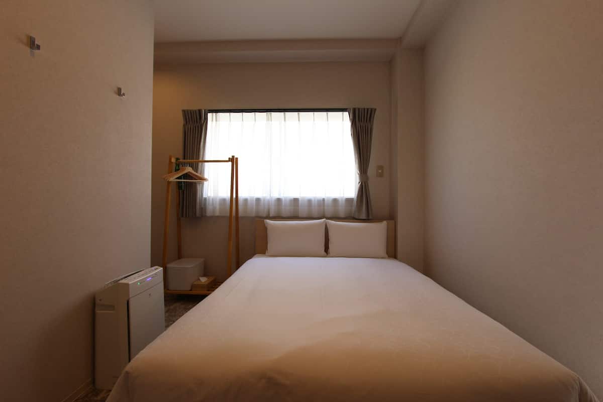 A hotel room with a bed, a bedside table, a lamp, and a window with curtains.