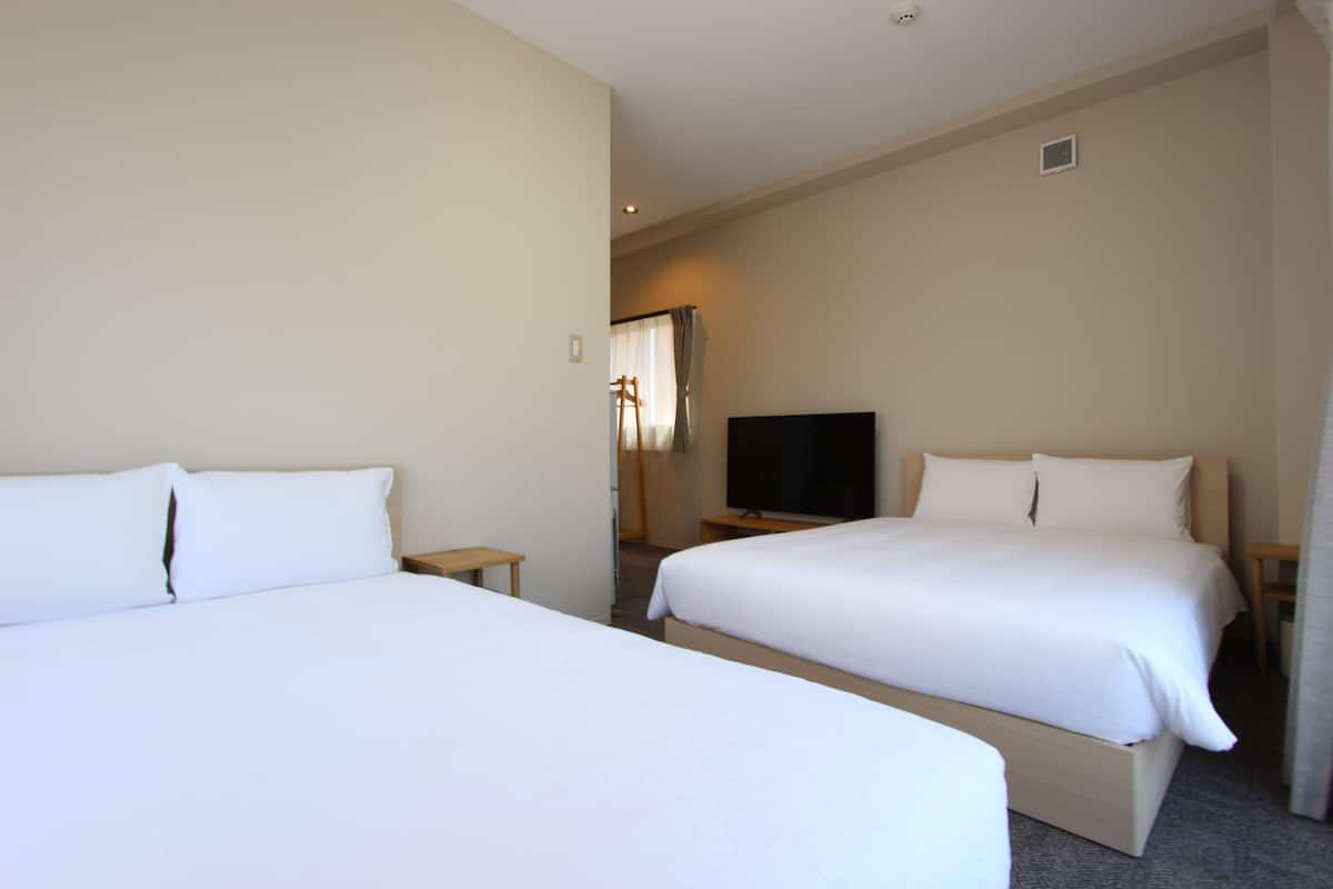 A hotel room with two single beds, a television, and a small table.