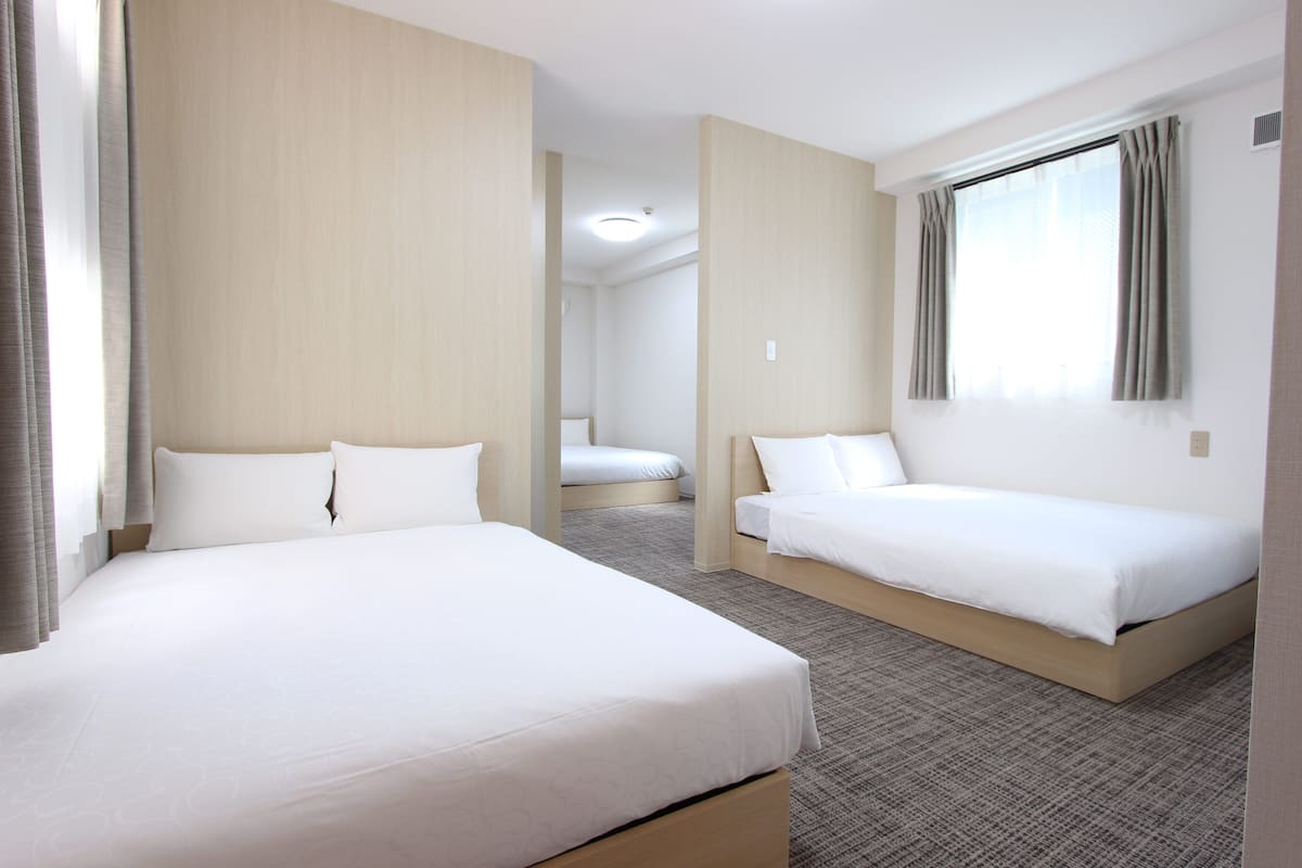 A hotel room with two beds, a large window with curtains, and a carpeted floor.