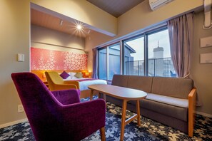 A hotel room with a bed, a sofa, a small table, and purple chairs.