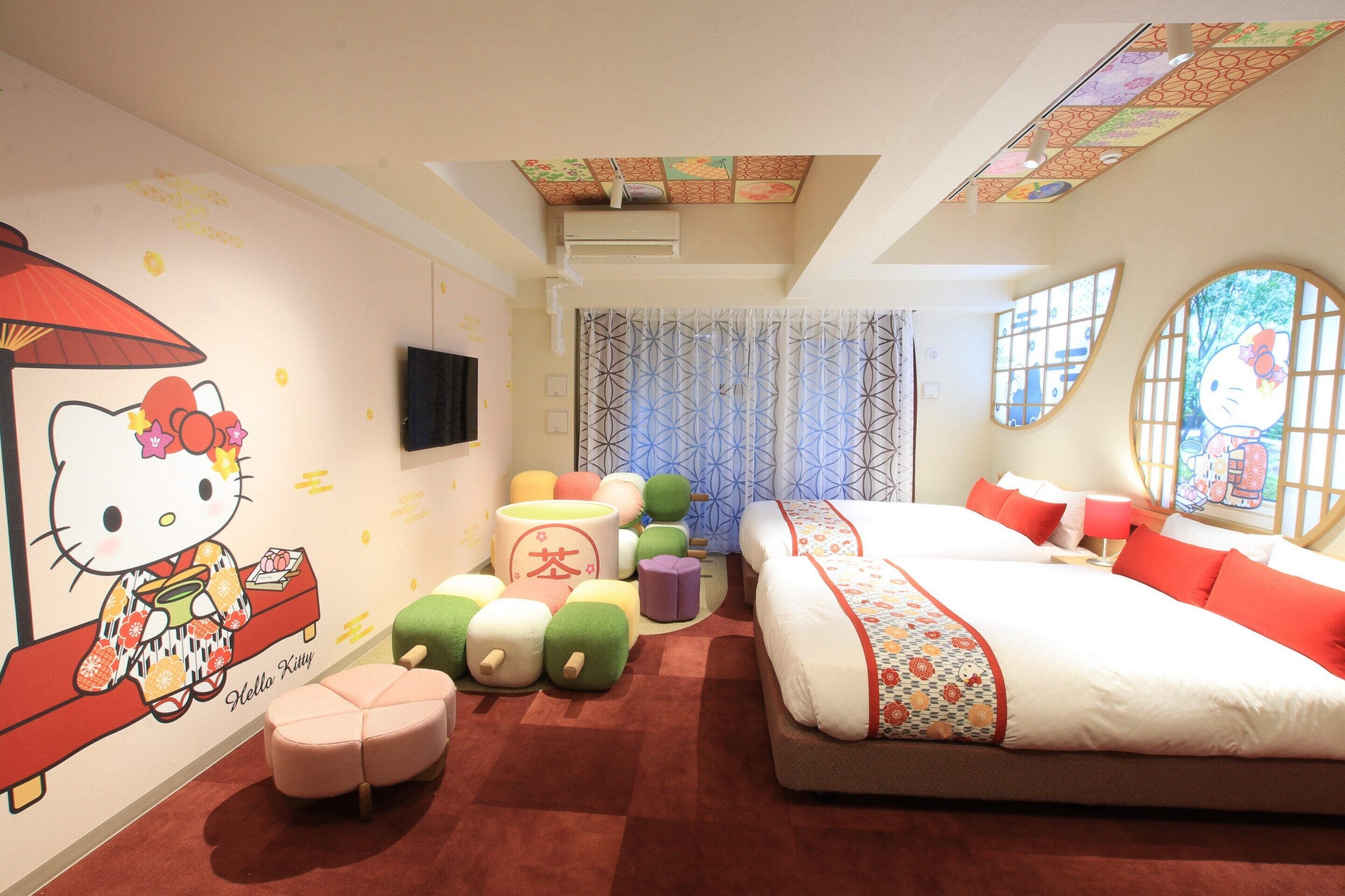 A children's room with a Hello Kitty mural, a bed with red and white bedding, and a window with a Hello Kitty design.