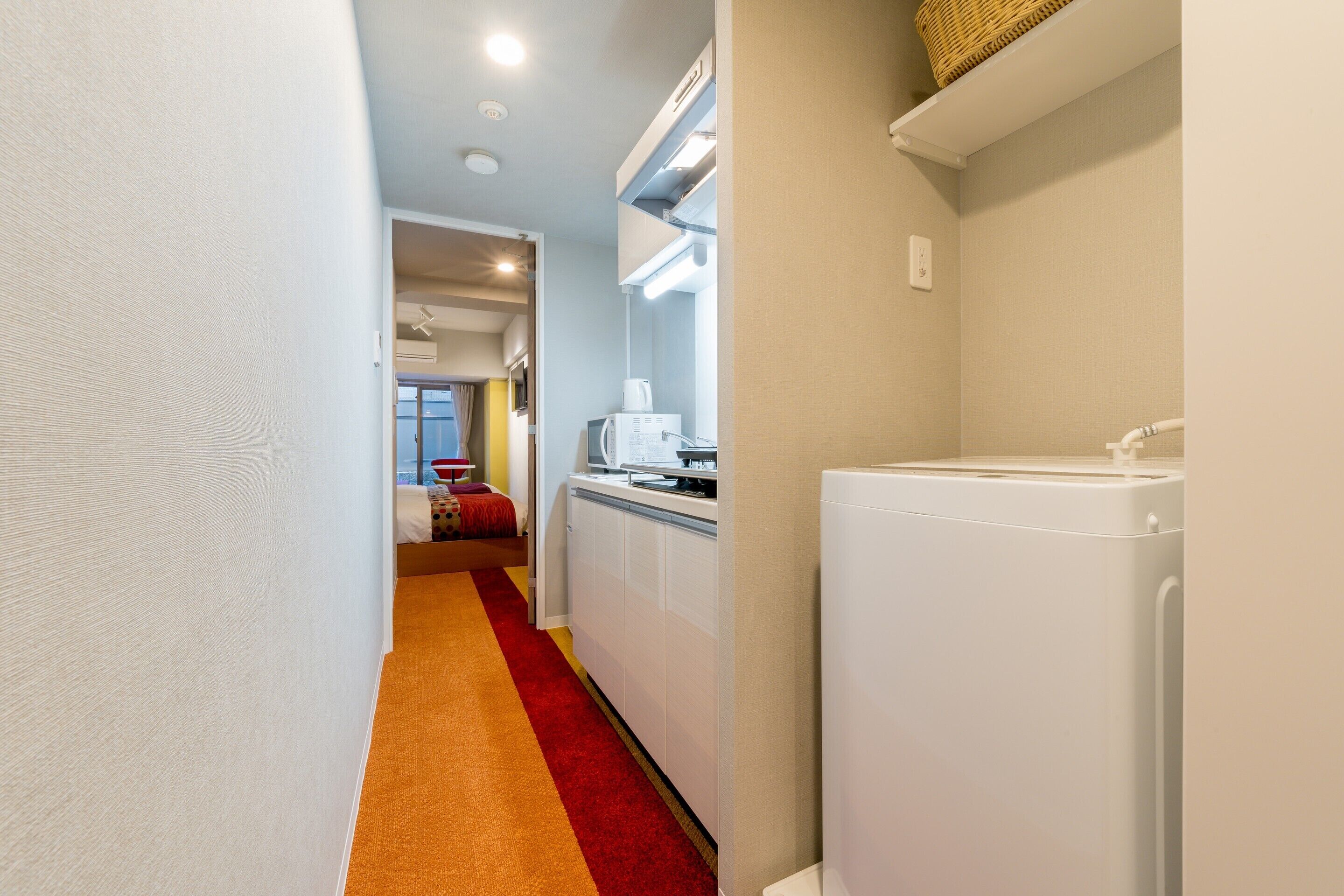 A narrow hallway with a red carpet, a white refrigerator, a microwave, and a small kitchenette area.