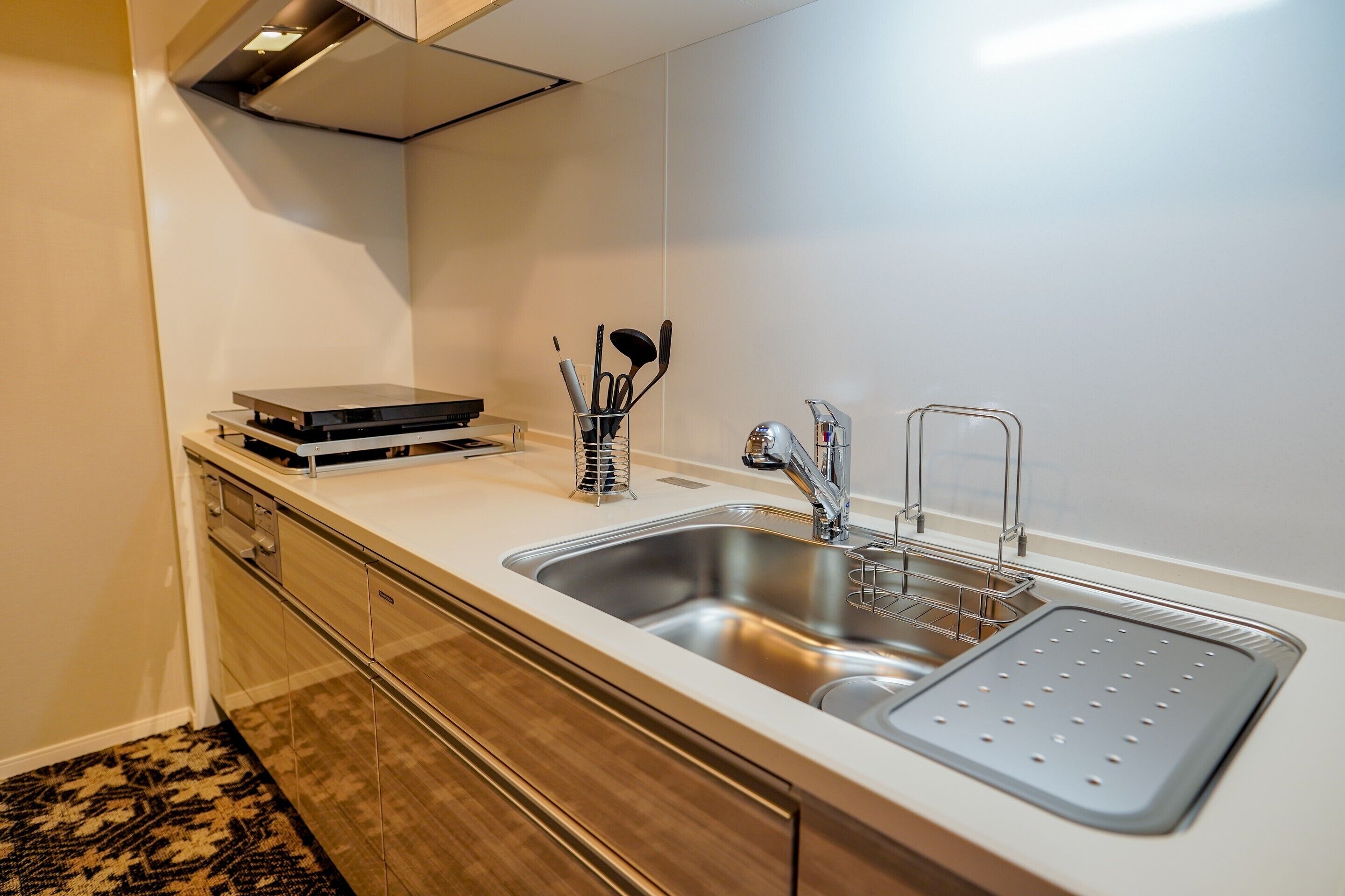 A modern kitchen with a stainless steel sink, a built-in oven, and a microwave. There is a utensil holder with various kitchen tools.