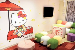 Une chambre décorée d’une fresque représentant Hello Kitty, dotée d’un téléviseur à écran plat et agrémentée de coussins colorés.
