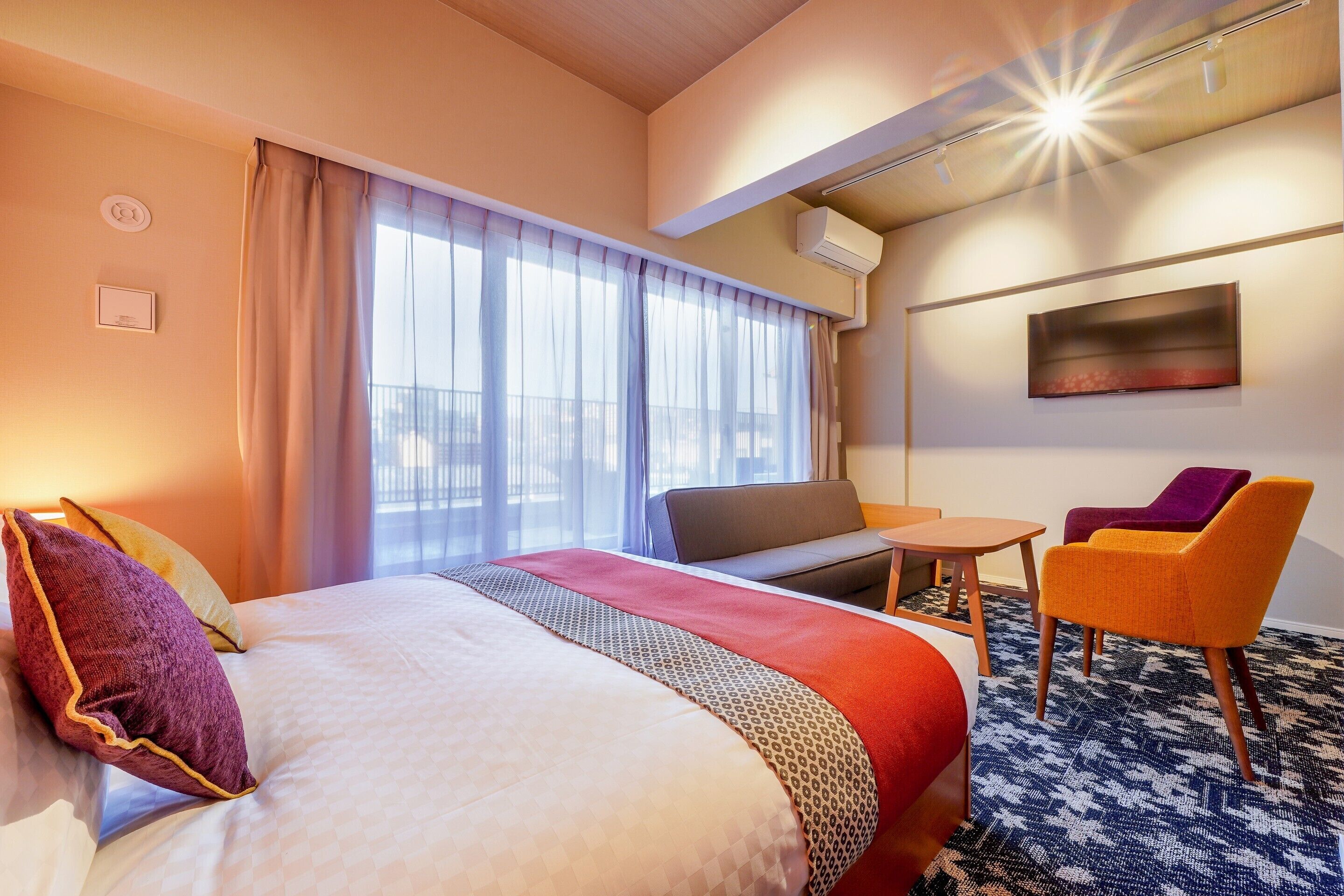 A hotel room with a bed, a sofa, a small table, and two chairs.