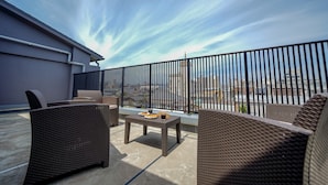 A rooftop terrace with wicker furniture, a table with plates and drinks, and a view of the cityscape. - RESI STAY THE KYOTO (Kyoto)