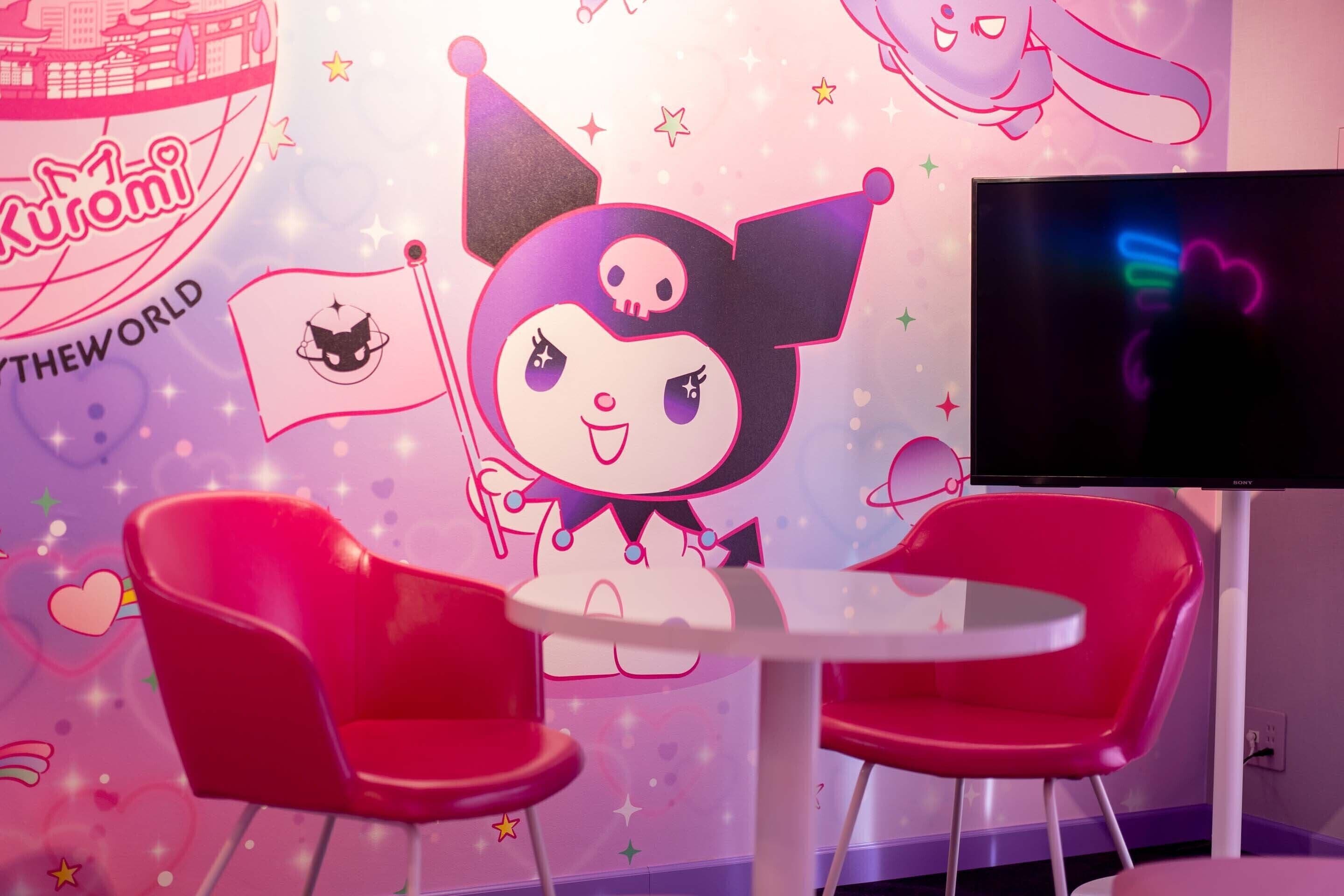 A room with a white table and two red chairs, a TV on the wall, and a wall decorated with cartoon characters and stars.