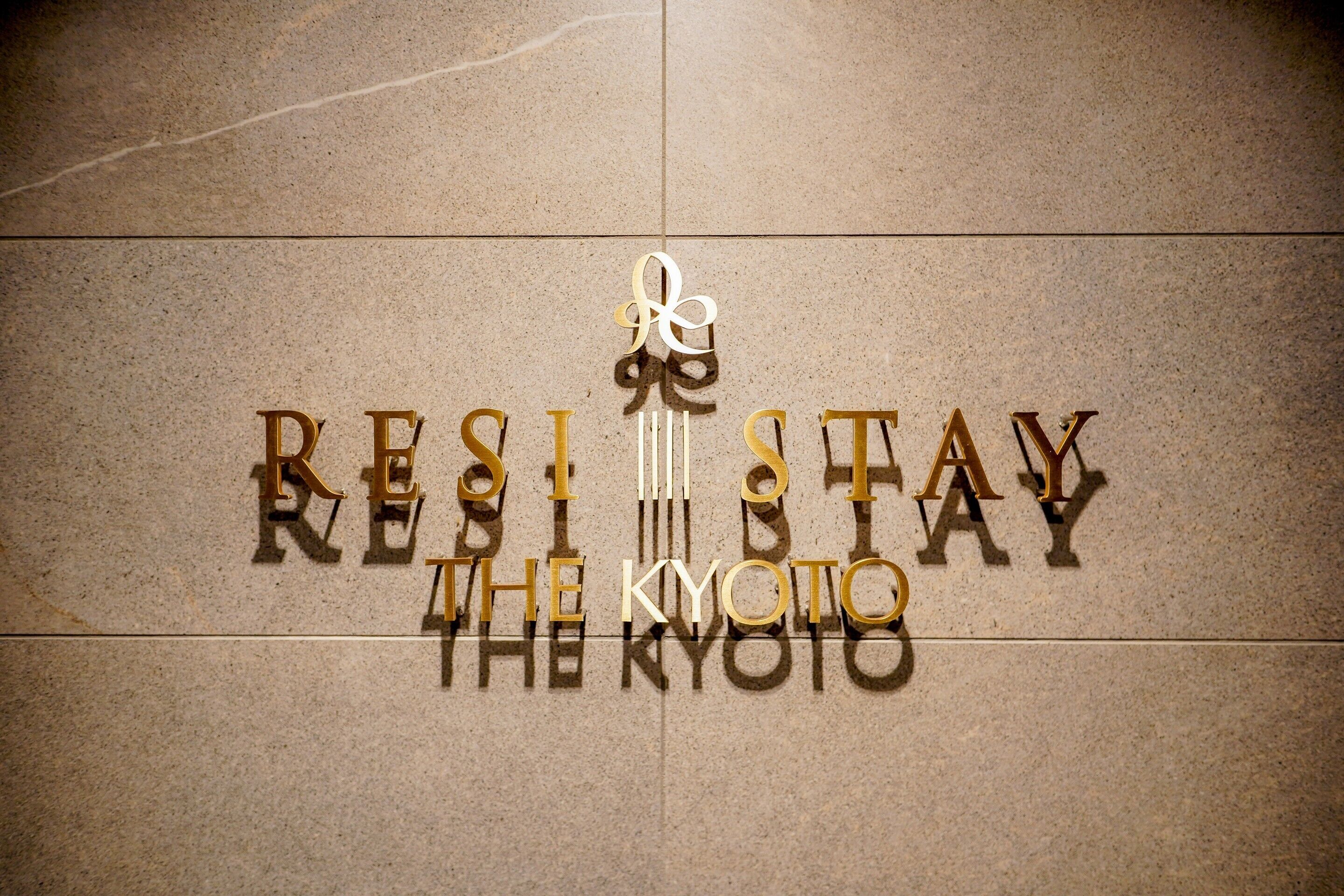 A sign with the words "RESIST STAY THE KYOTO" in gold lettering on a stone surface.