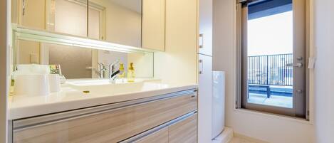 A modern bathroom with a large mirror, white sink, and a window with a balcony view.