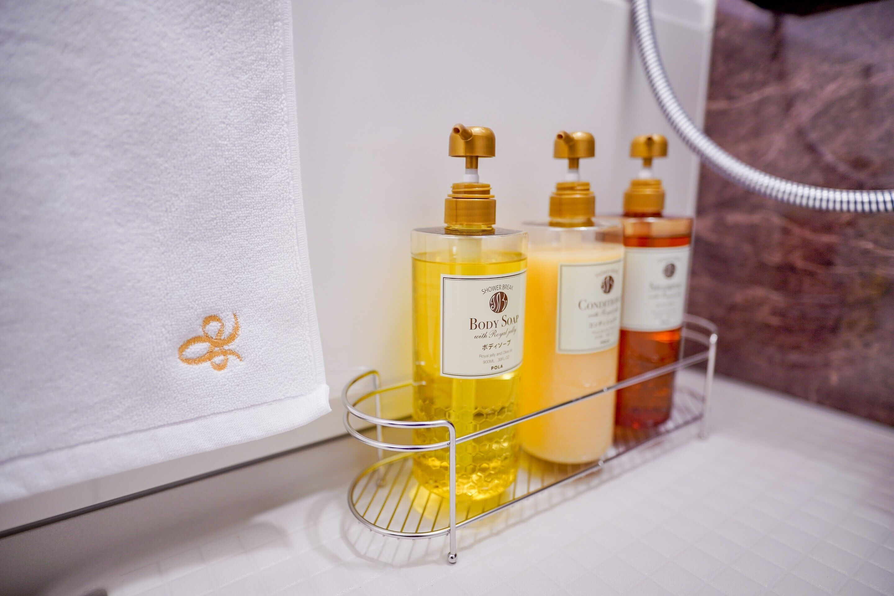 A bathroom shelf with three bottles of body soap and a shower hose.