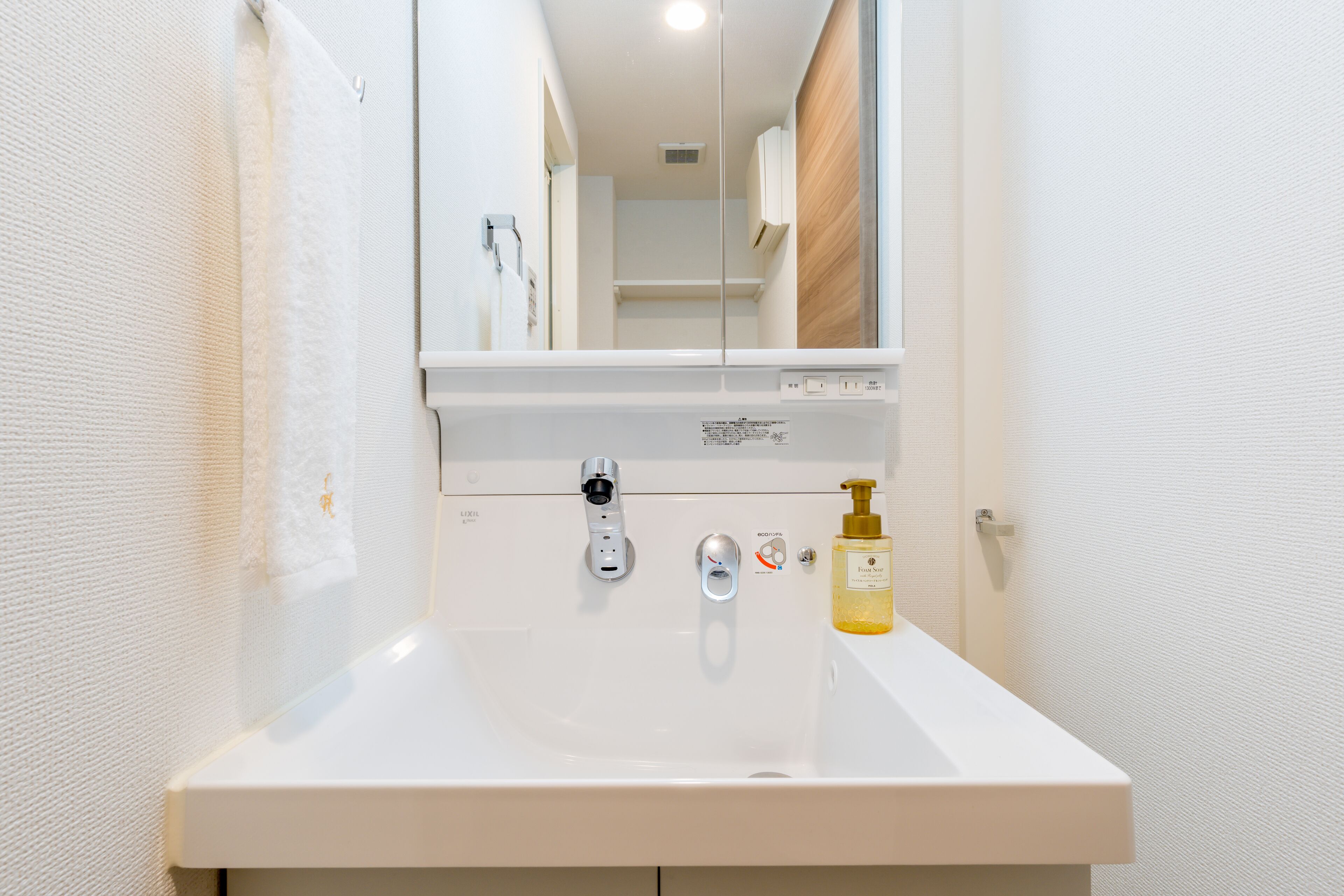 A modern bathroom with a white sink, a mirror, and a bottle of hand soap.