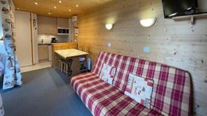 Interior acolhedor de uma cabana com teto de madeira, uma cozinha compacta, um espaço de refeições e um sofá com manta xadrez.