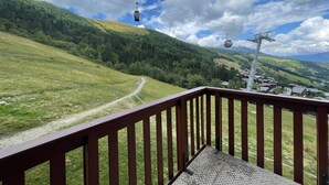 Uma varanda com vista para uma paisagem montanhosa, uma trilha de terra e um sistema de teleférico.