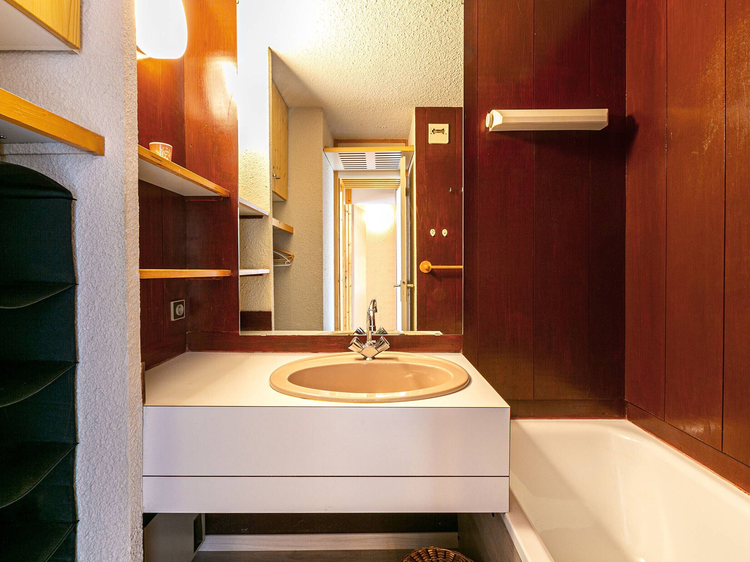 Ein Badezimmer mit einem weißen Waschbecken, einem Spiegel und einer Holztür.