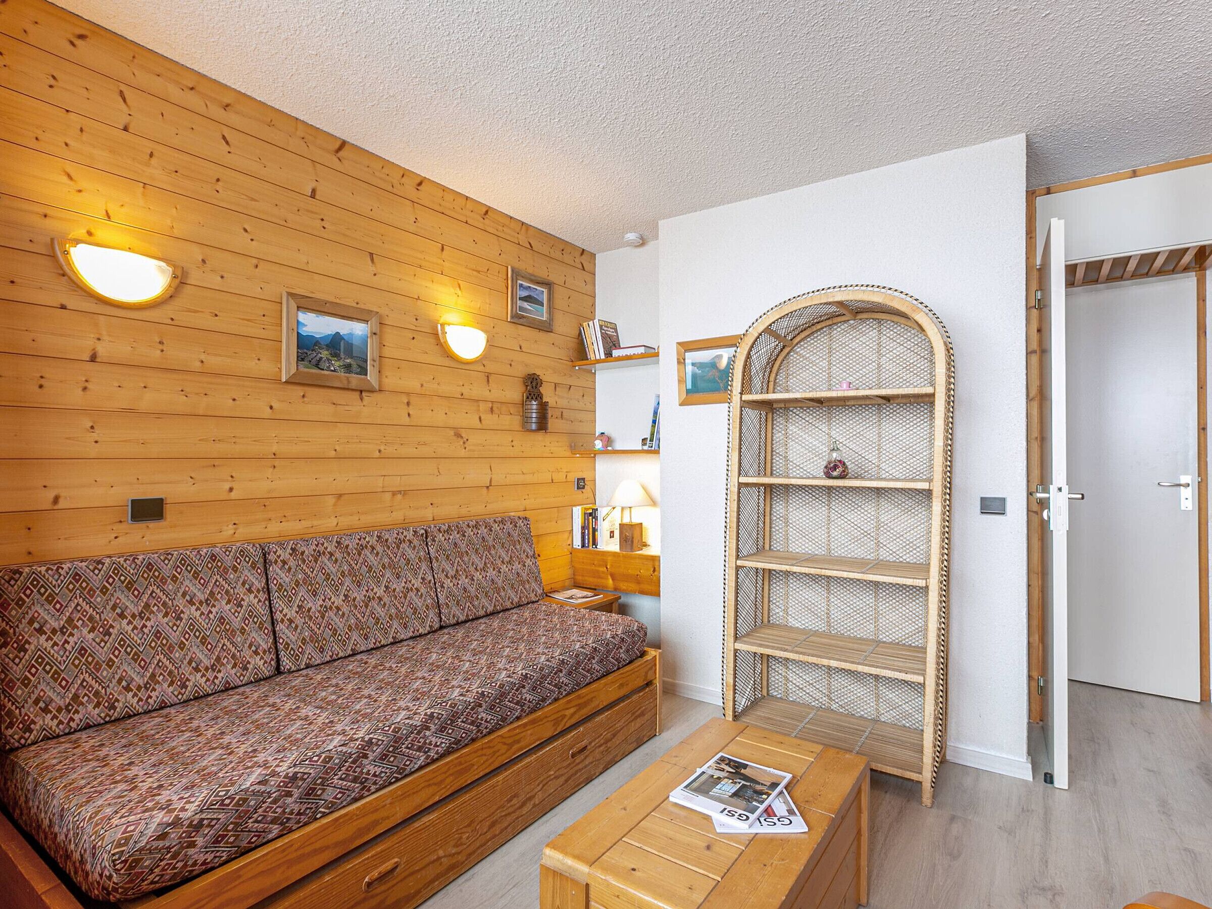 A cozy room with a wooden wall, a patterned sofa, a wooden coffee table, and a wicker shelf.