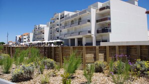 A multi-story hotel with balconies, a wooden fence, and a landscaped garden with various plants. - Cozy Appart 150 m from the beach with balcony + Parking (Biscarrosse)
