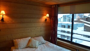 A hotel room with a wooden headboard, two bedside lamps, a bed with white linens, and a window with a view of buildings.