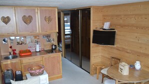 A compact kitchen with wooden cabinets, a sink, and a television mounted on the wall.