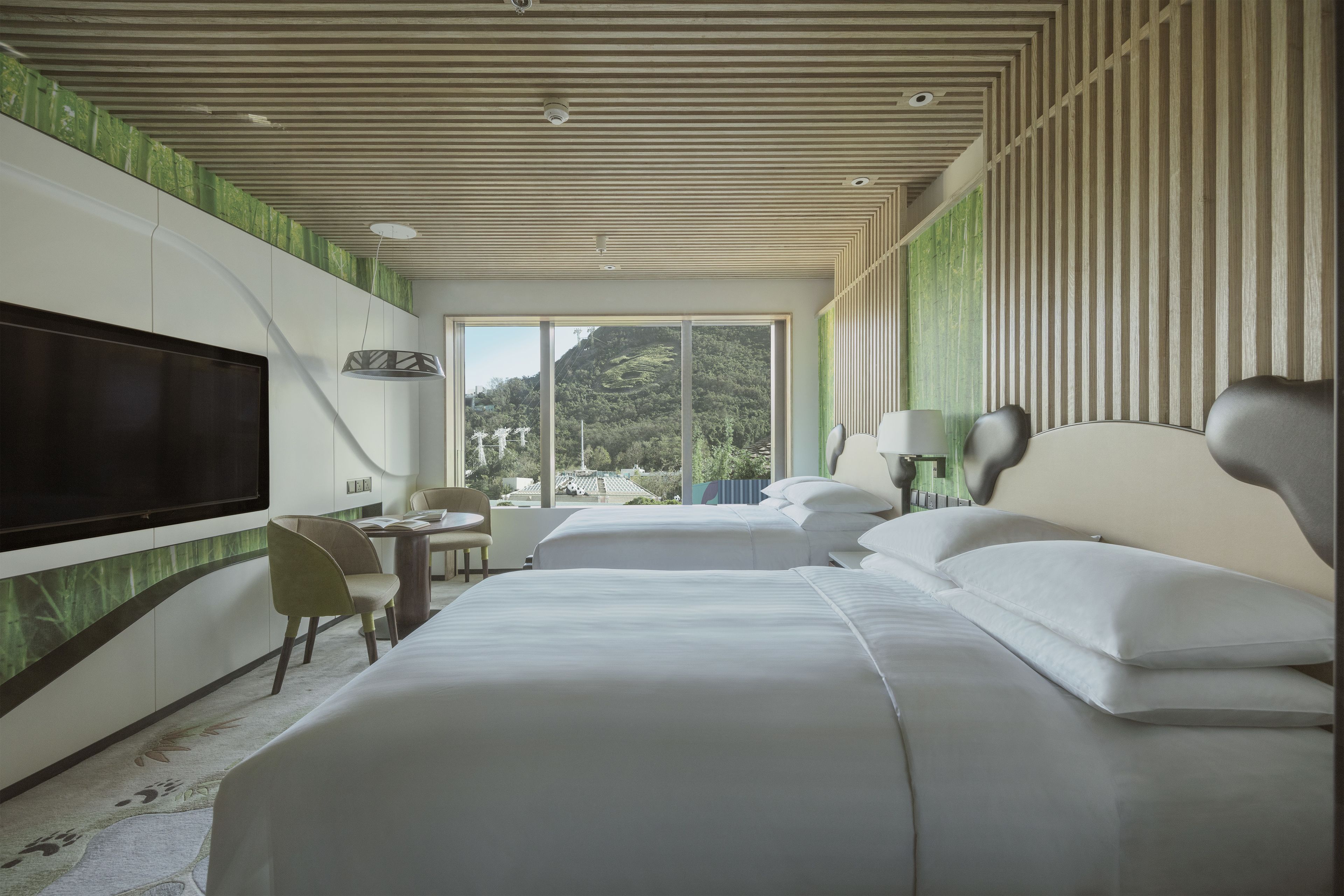 A modern hotel room with a large bed, a TV, a desk, and a view of a mountainous landscape.