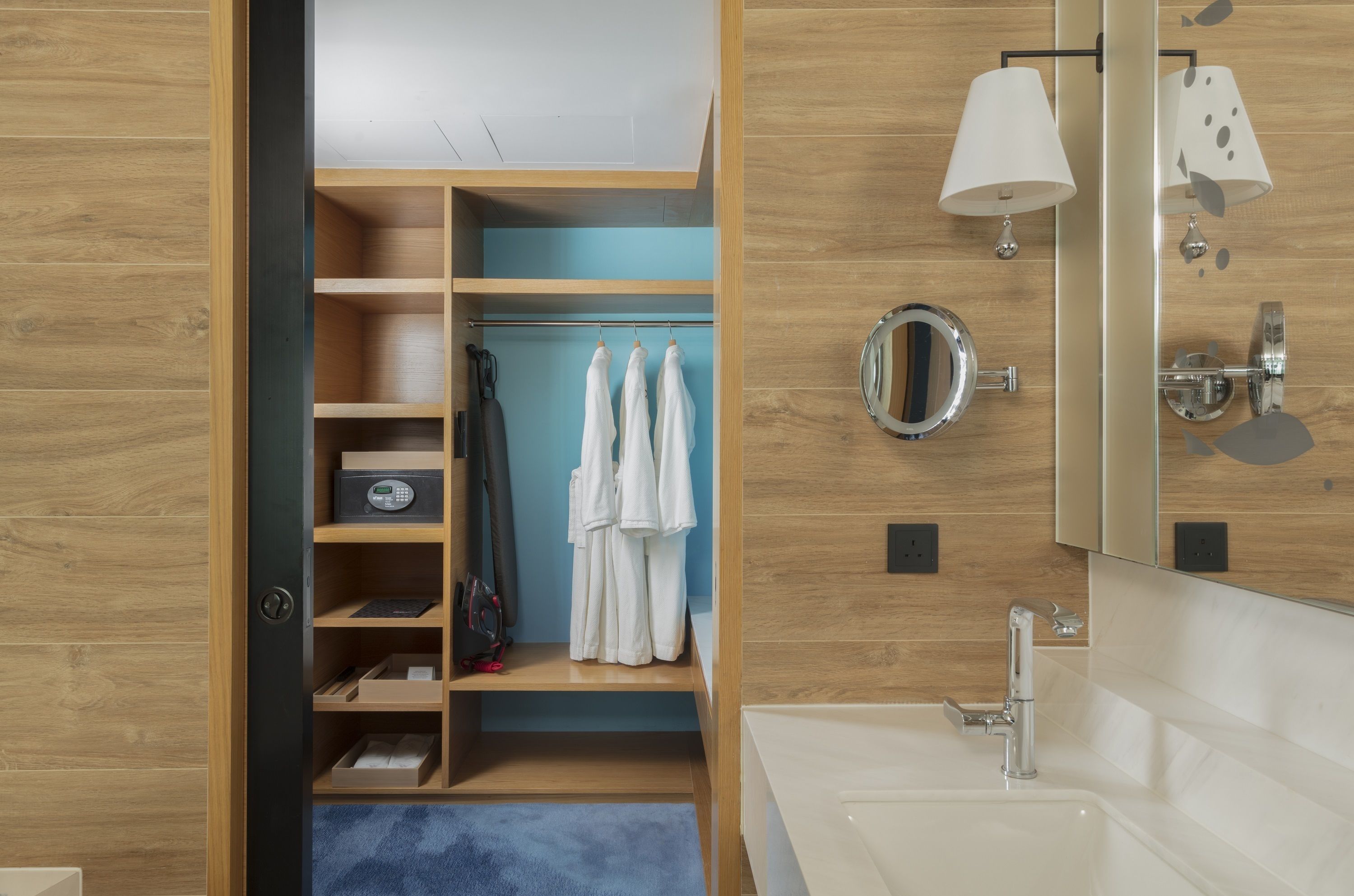A modern bathroom with a wooden vanity, a large mirror, and a built-in towel rack.