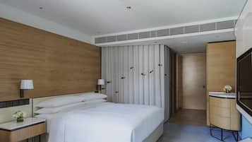 Een moderne hotelkamer met een groot bed, nachtkastjes, een televisie, een houten kledingkast en een badkamer met een wastafel en spiegel.