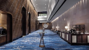 A hotel corridor with a blue patterned carpet, a reception desk with a bar, and a modern brick wall on the left. - Hong Kong Ocean Park Marriott Hotel (Hong Kong)