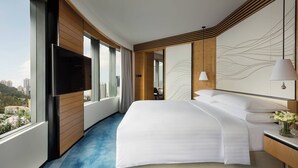A modern hotel room with a large bed, a flat-screen TV mounted on the wall, a desk with a lamp, and a view of the city through large windows. - Hong Kong Ocean Park Marriott Hotel (Hong Kong)