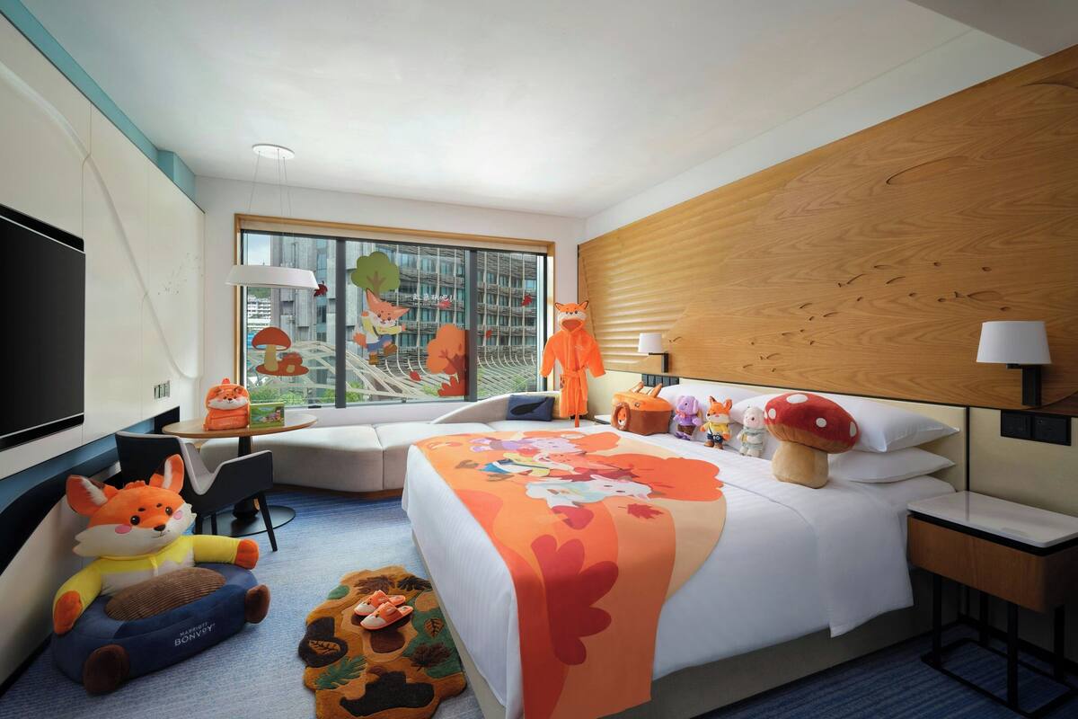 A hotel room with a large bed, a sofa, a TV, and a window with a view of buildings.