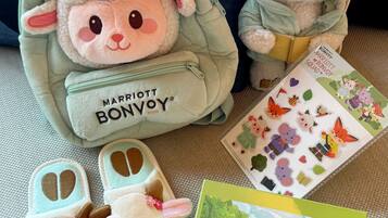 Um brinquedo de pelúcia dentro de uma bolsa verde com a inscrição 'Marriott Bonvoy', um par de chinelos e uma caixa de quebra-cabeça.