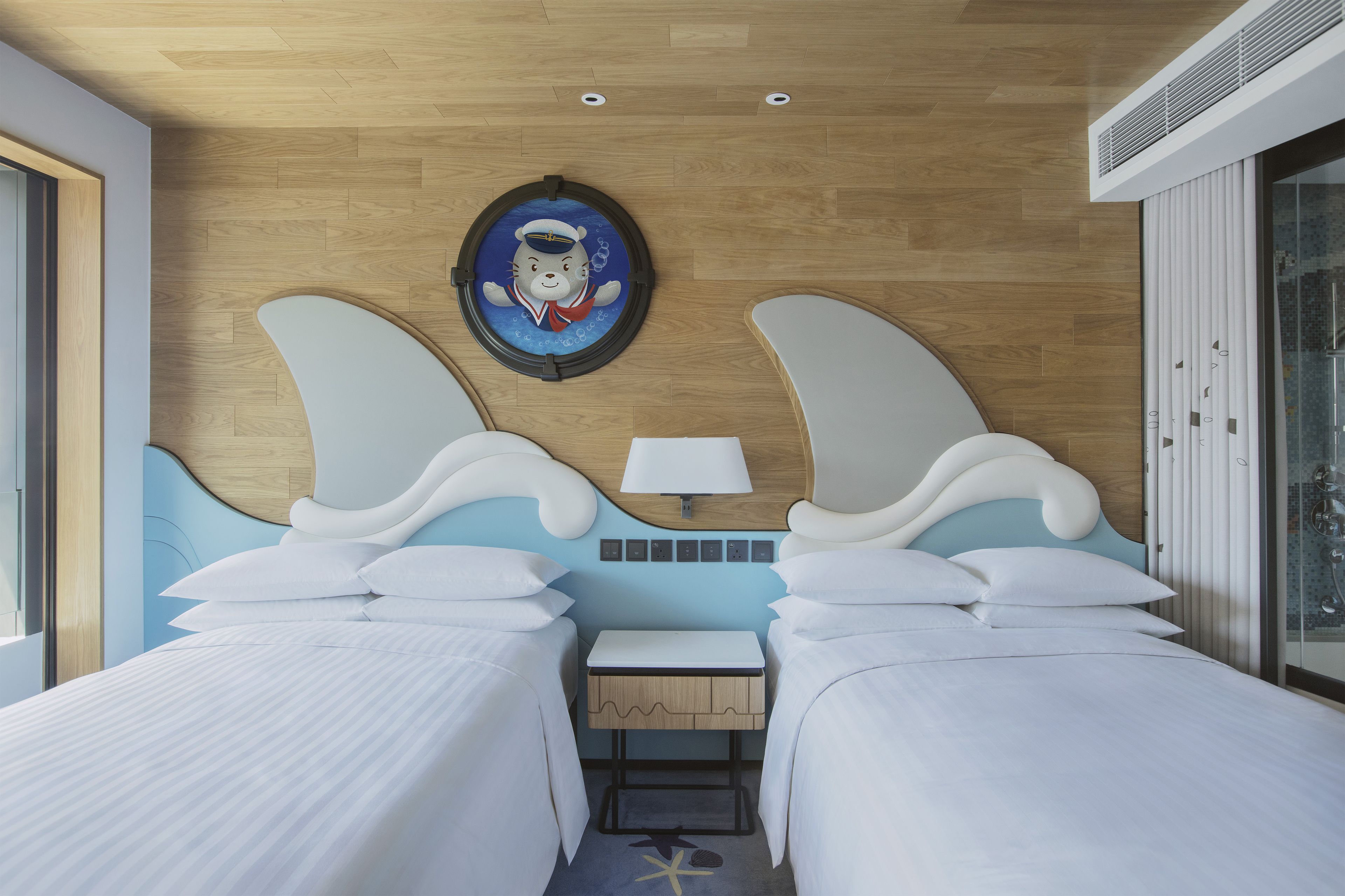 Habitación de hotel con dos camas, una mesita de noche pequeña, una lámpara de pared y un adorno mural.
