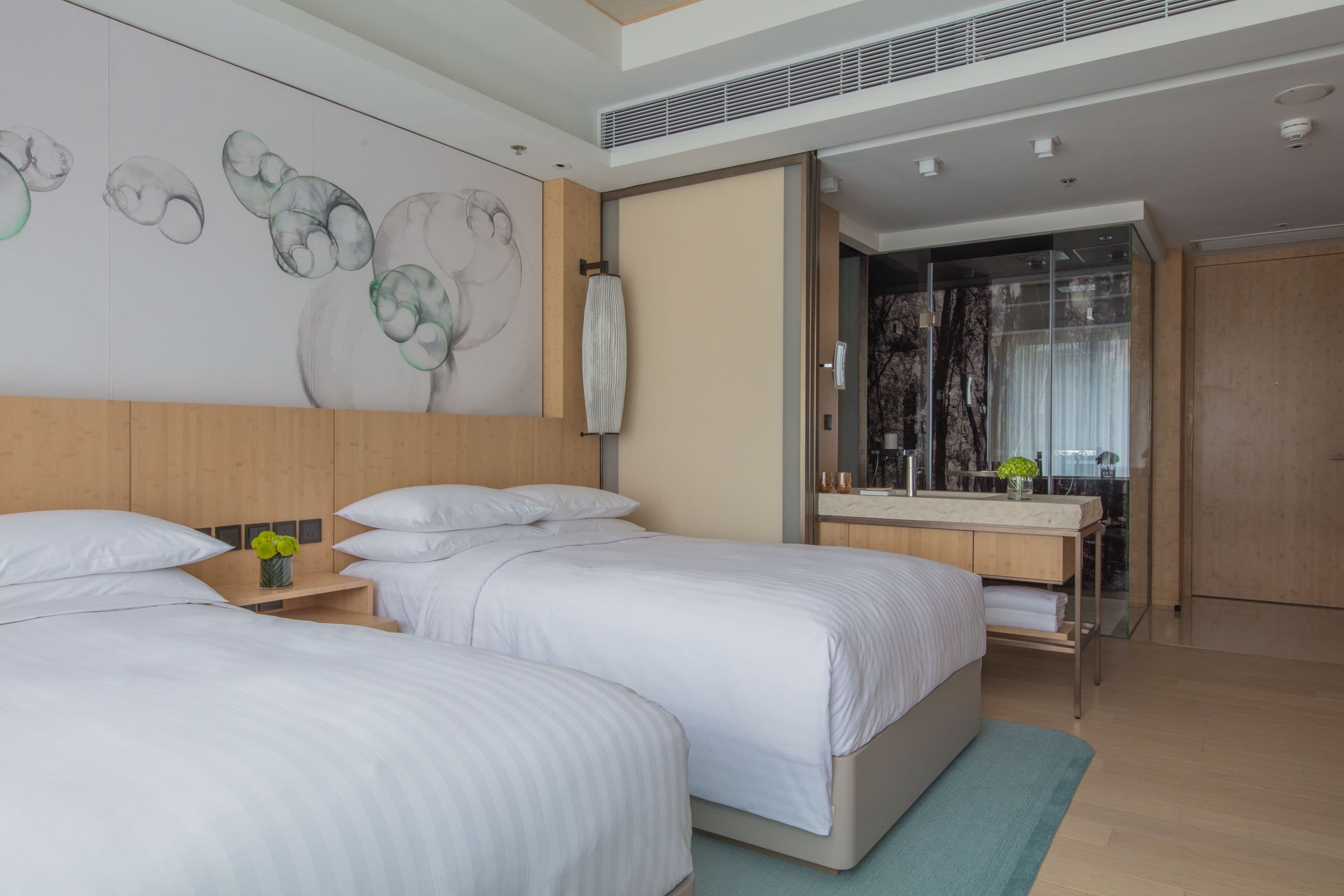 A modern hotel room with two beds, a large mirror, and a bathroom with a shower and toilet.