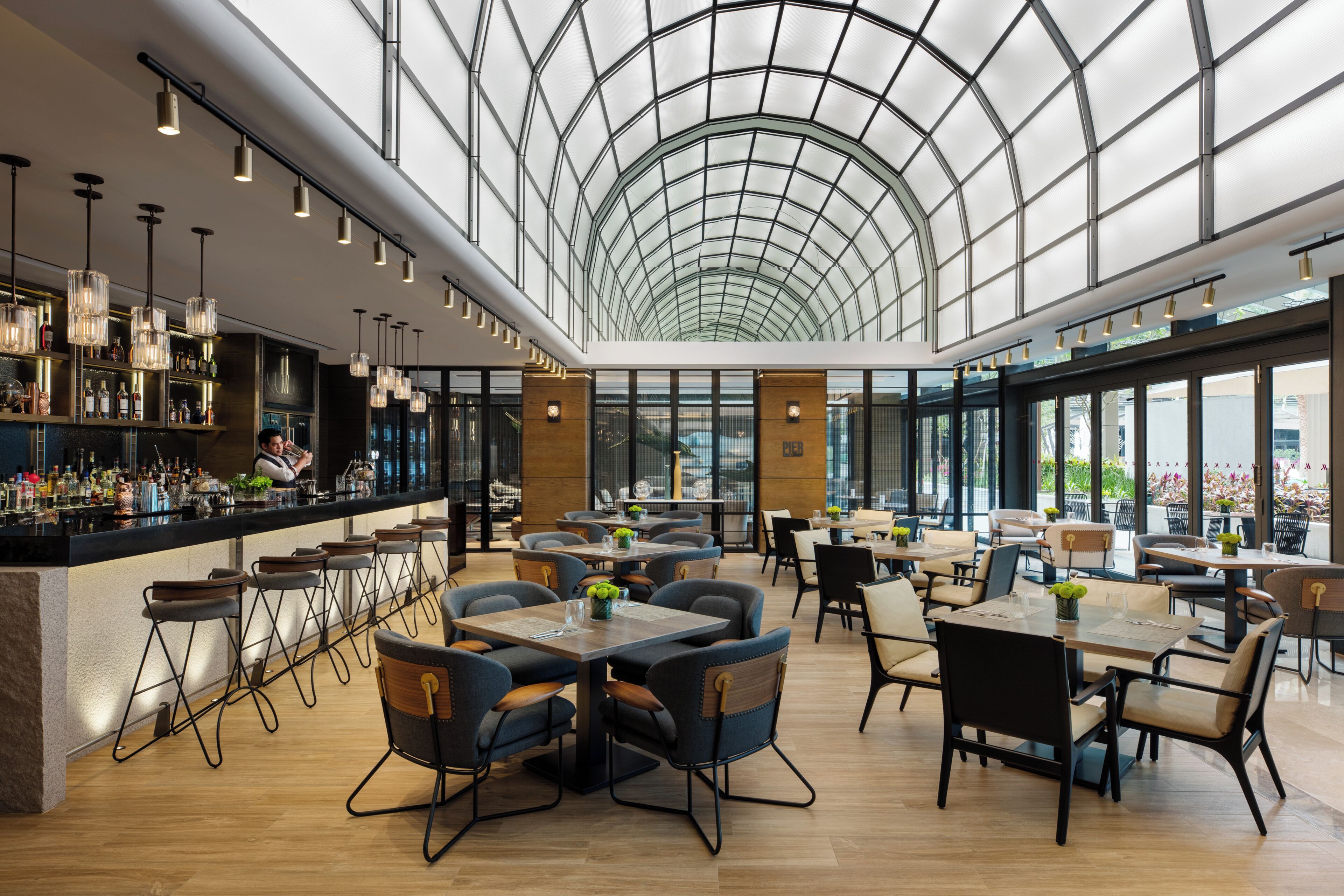 A spacious indoor area with a high ceiling and a glass dome structure. There are tables and chairs arranged for dining, and a bar area with bottles and glasses.