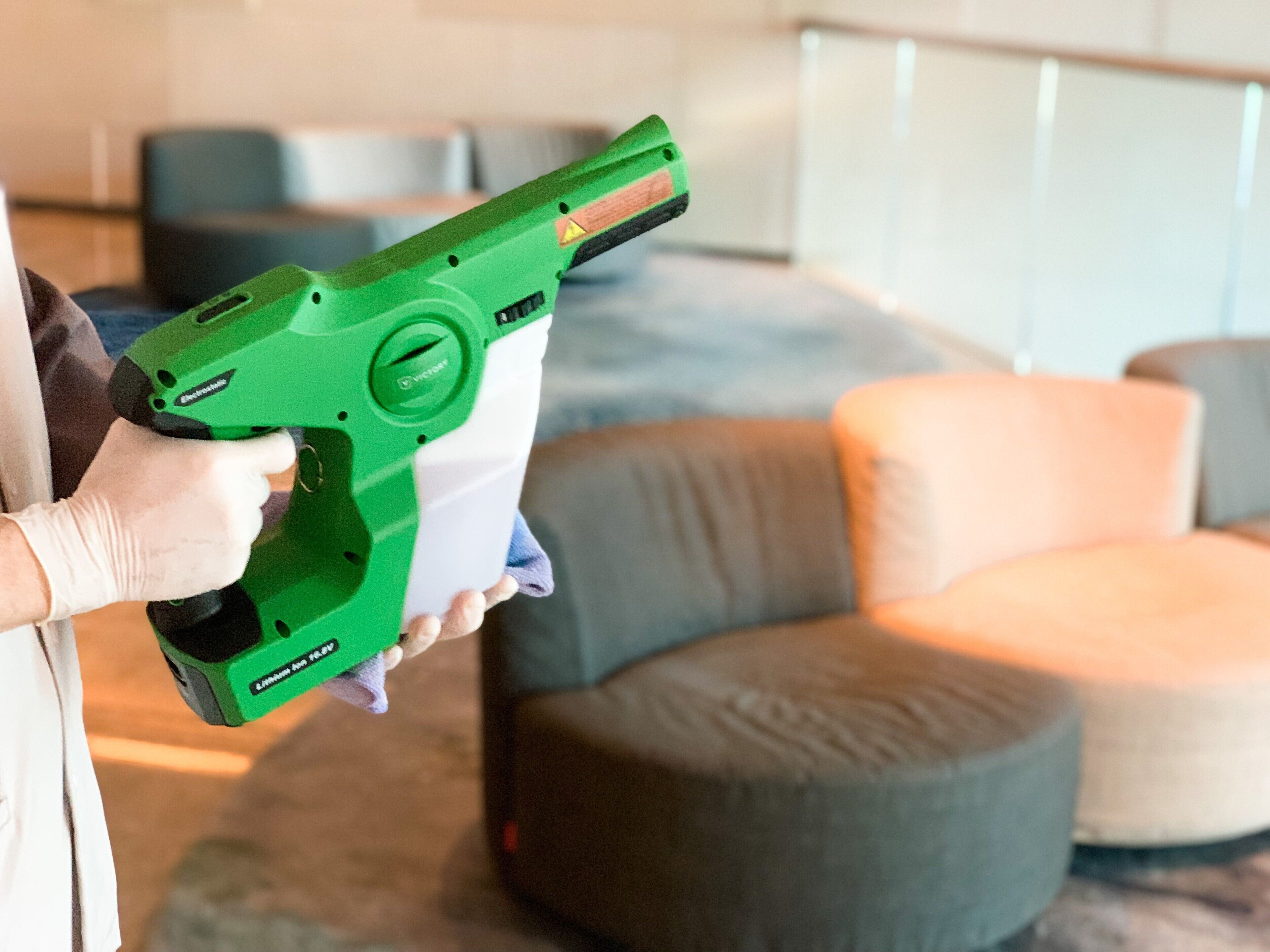 Una persona sostiene un dispositivo verde, posiblemente una herramienta de limpieza, en una habitación moderna con muebles grises y beige.