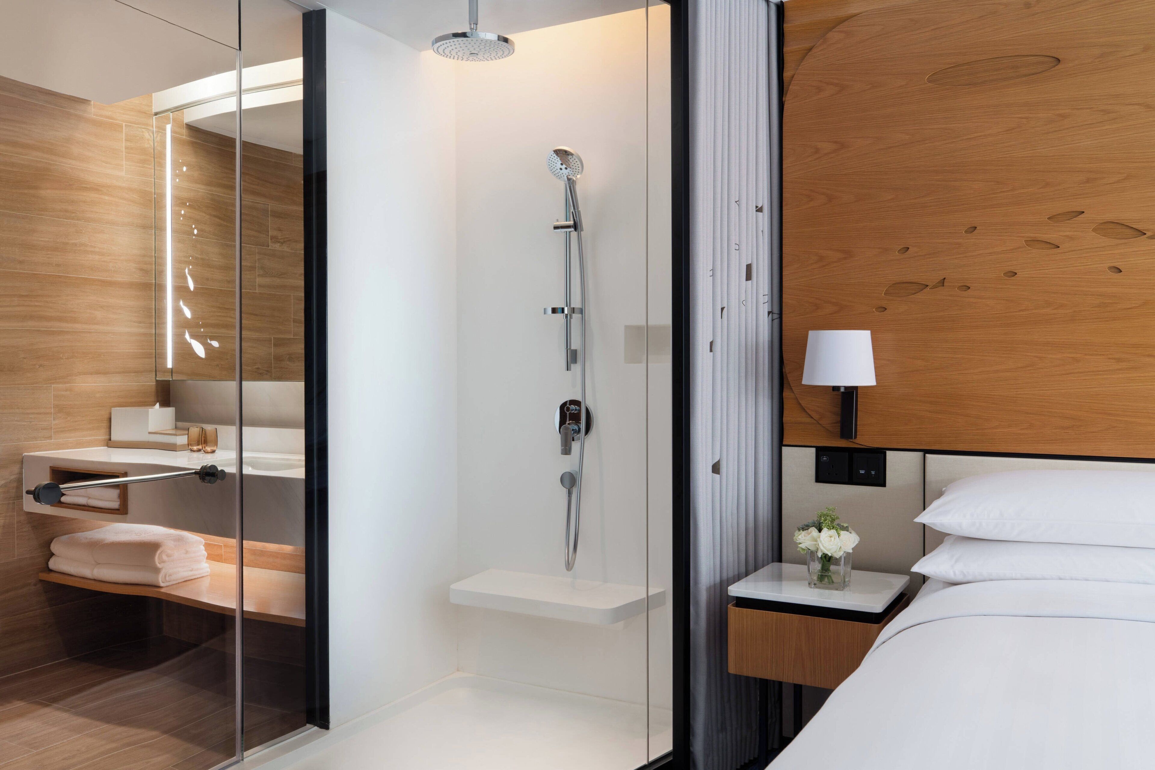 Une salle de bain moderne avec une douche à l’italienne en verre, un lavabo blanc et un meuble-lavabo en bois.