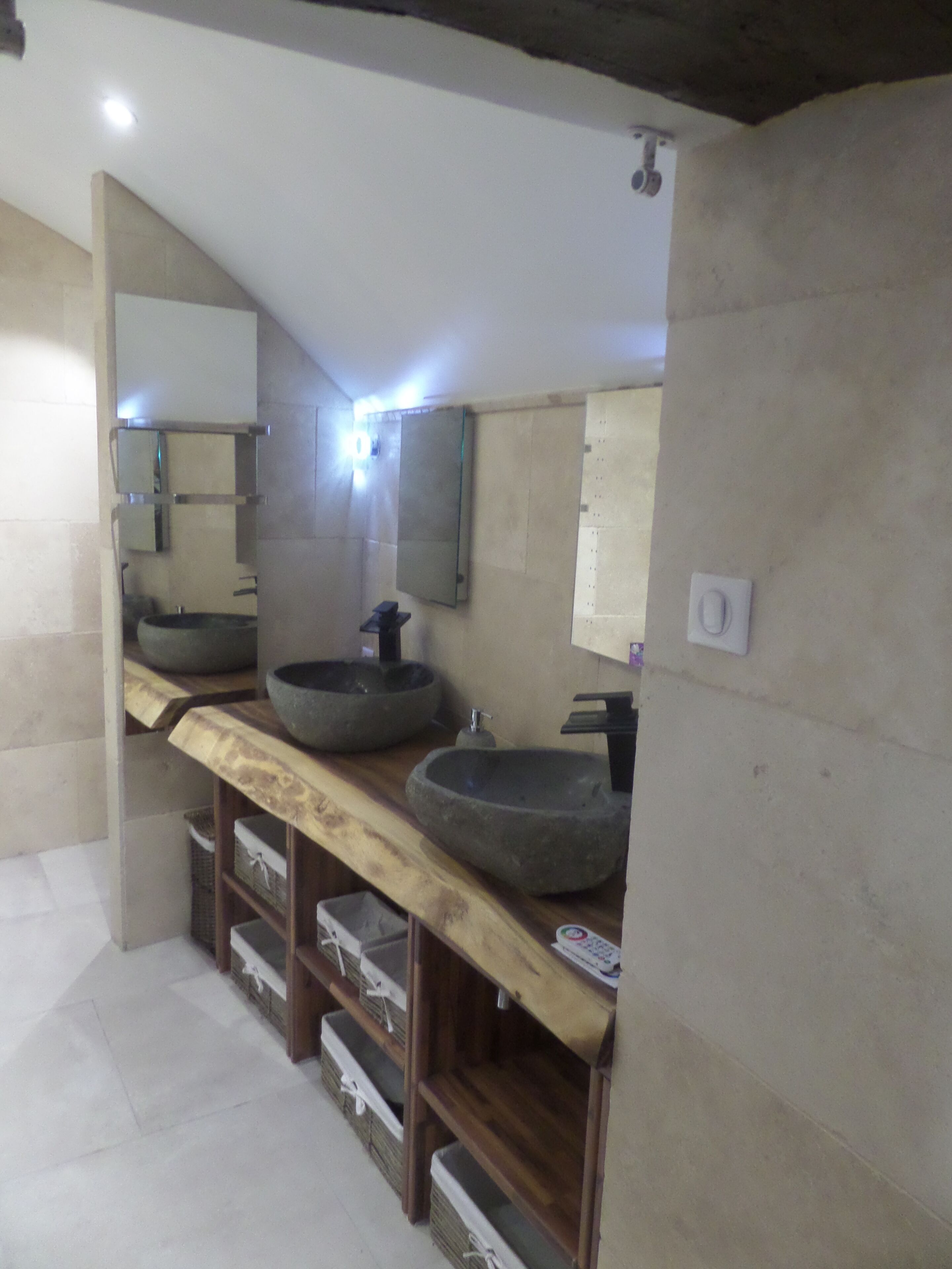 Une salle de bain avec un meuble-lavabo en bois, deux vasques en pierre et un grand miroir.