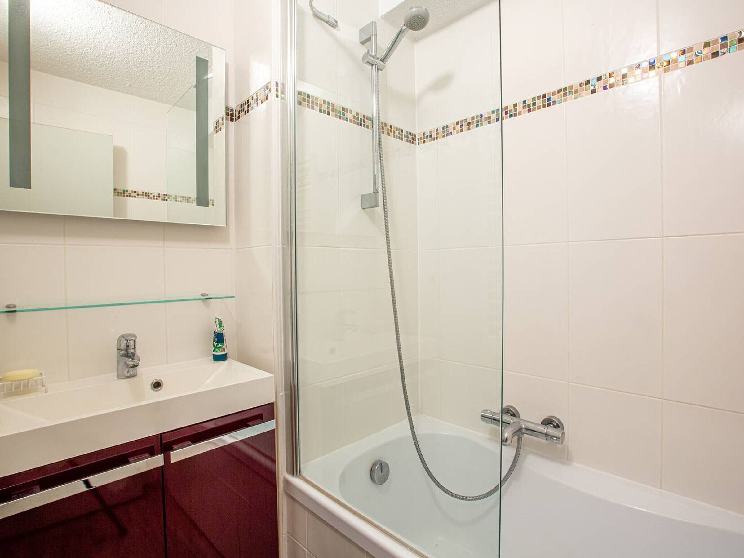 Une salle de bain avec une douche à parois de verre, un lavabo blanc et un miroir au-dessus du lavabo.