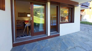 A modern building with large sliding glass doors leading to a room with a bed and a table. - Valmorel - Cozy apartment for 4, direct access to slopes (Valmorel)