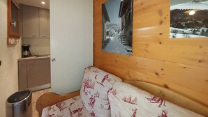 A cozy room with a wooden ceiling, a sofa with a ski-themed cover, and two framed pictures depicting snowy landscapes. - Valmorel - Cozy apartment for 4, direct access to slopes (Valmorel)