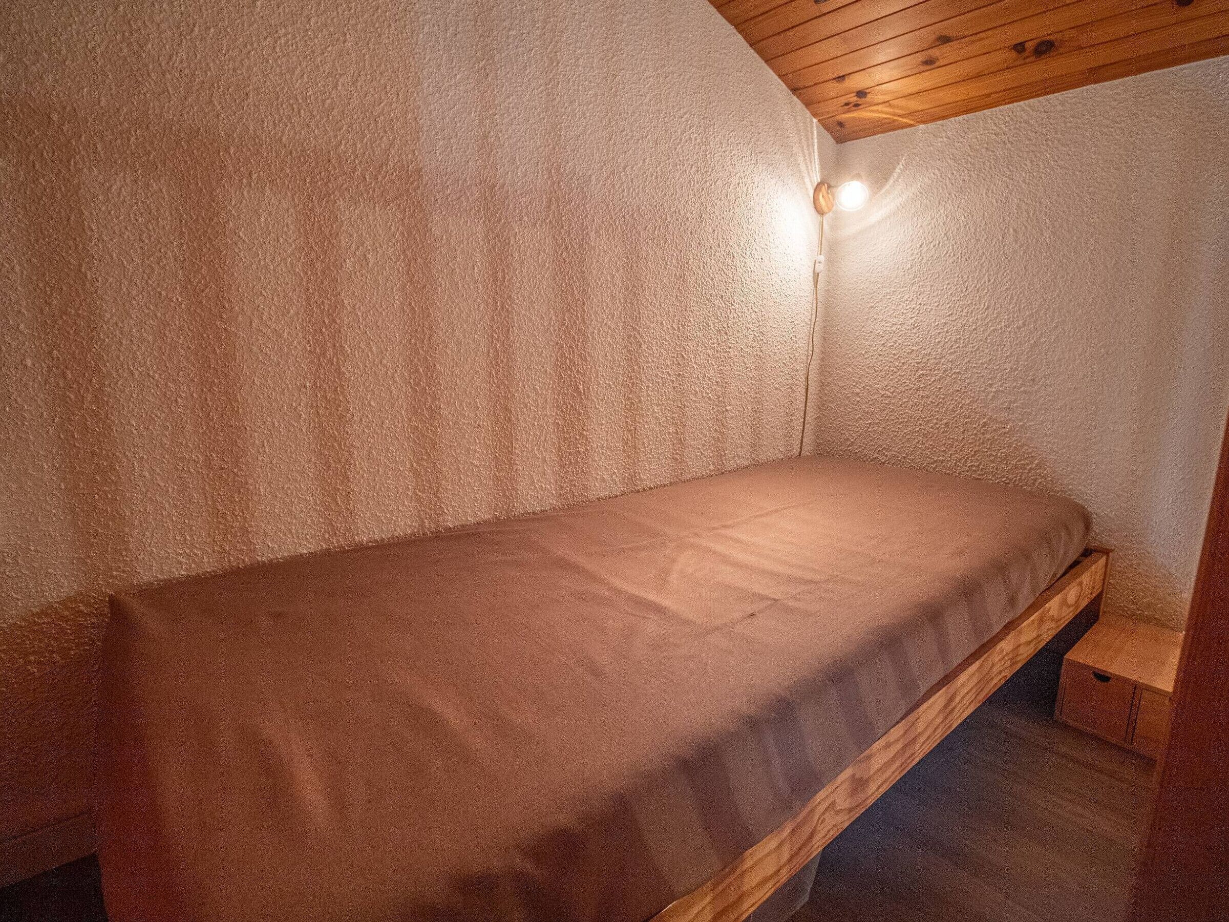 Une petite chambre avec un lit simple, un plafond en bois et un luminaire fixé au mur.