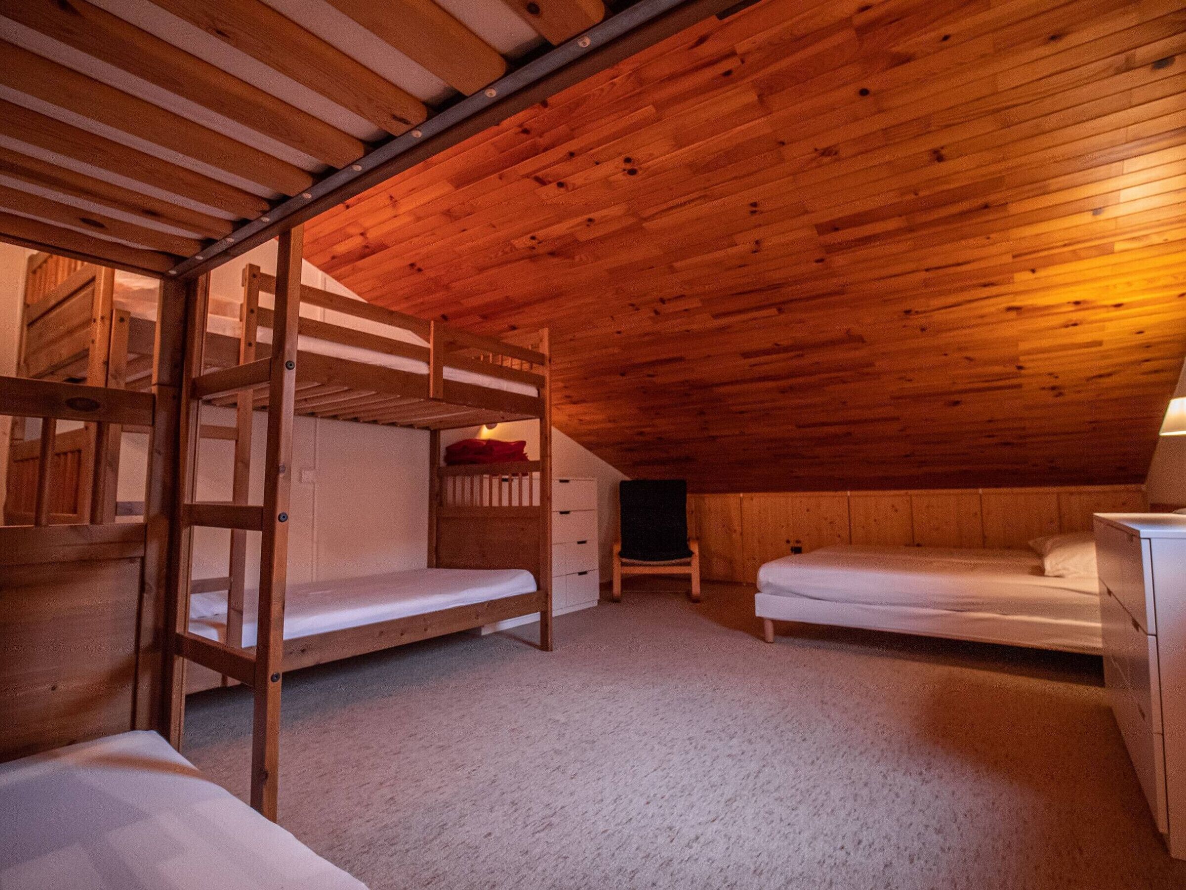 Une chambre mansardée chaleureuse avec des lits superposés en bois, un petit bureau et une chaise.